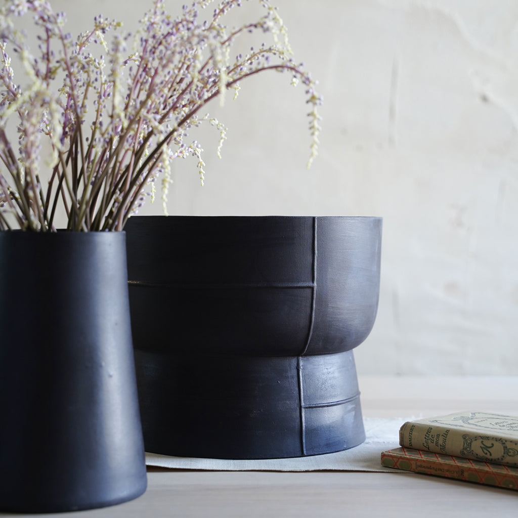 Handmade black ceramic pedestal bowl held by hand, minimalist stoneware decor centerpiece