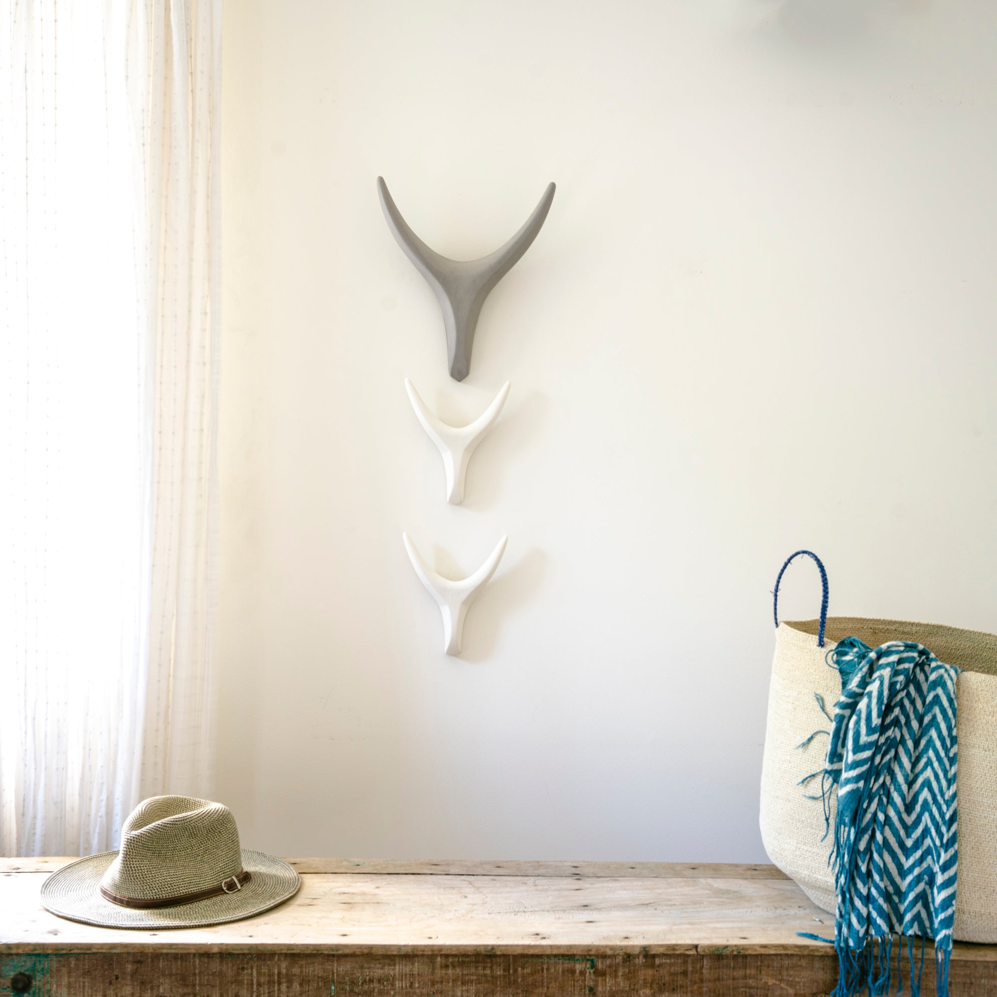 Decorative wall art with antlers above a wooden bench and chair with a blue patterned blanket.