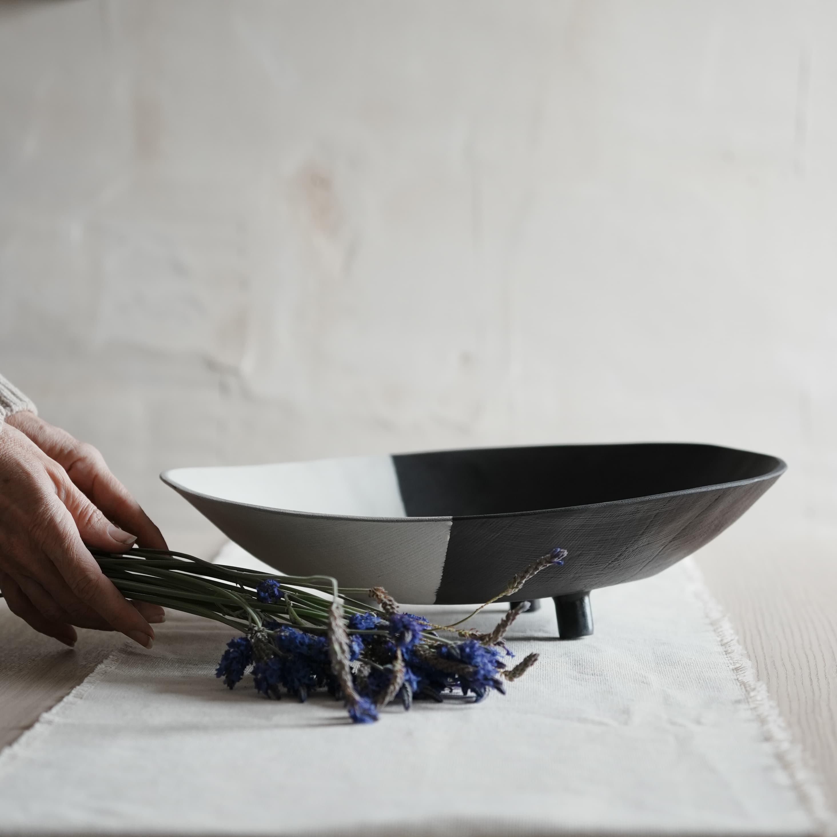 Person holding lavender near a black and white bowl on a light surface.