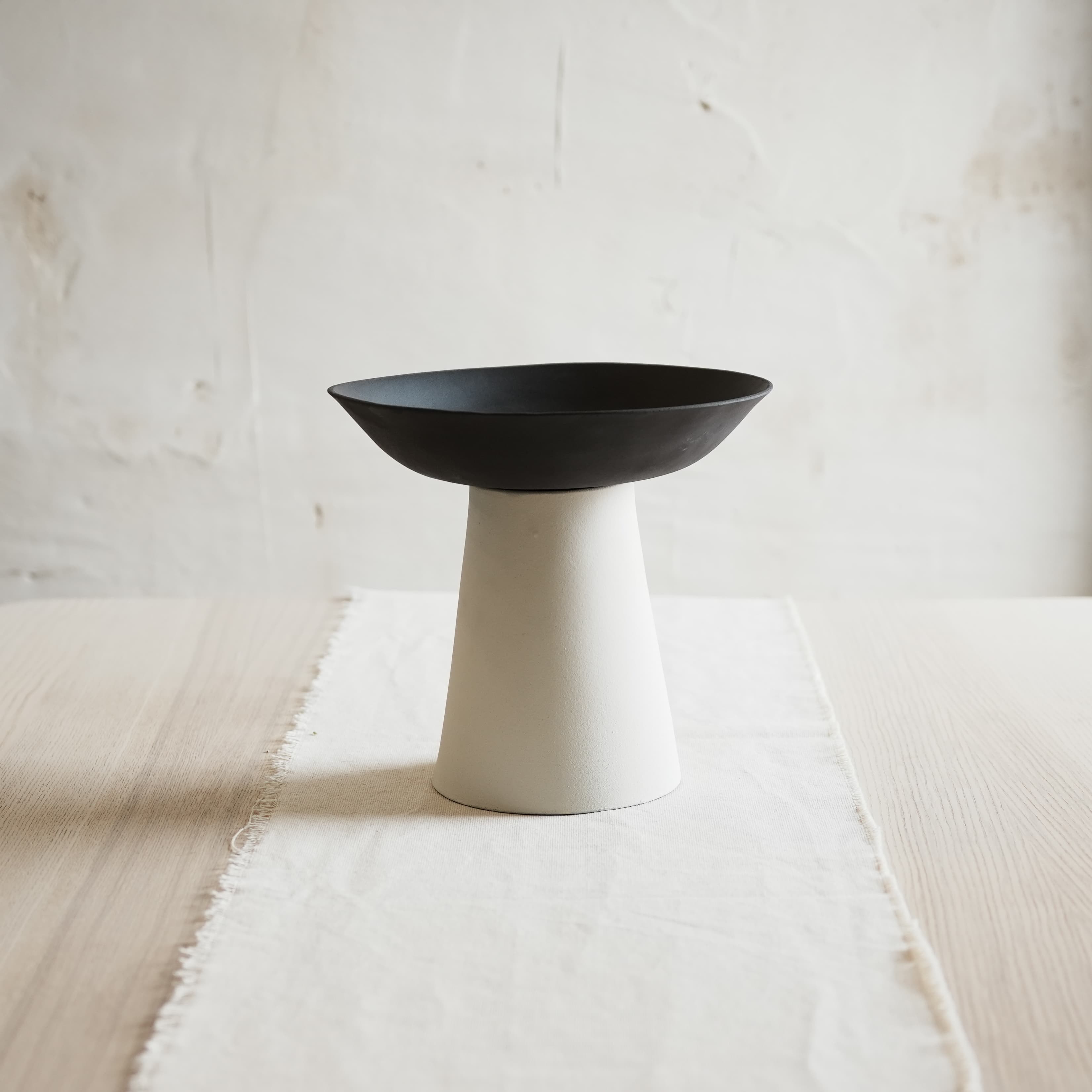Black bowl on a white pedestal vase against a light wooden background