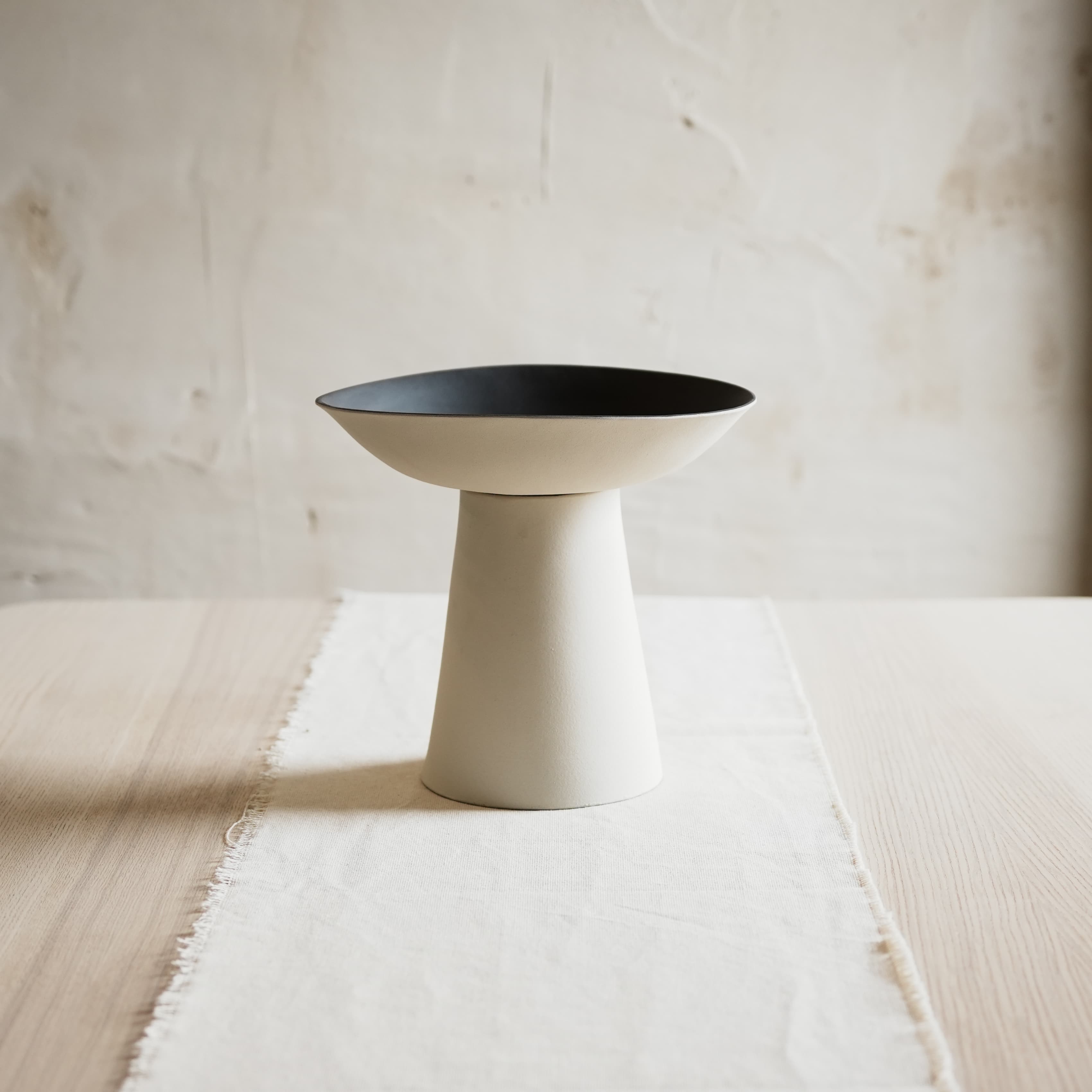 white vase with black bowl on a light wooden table