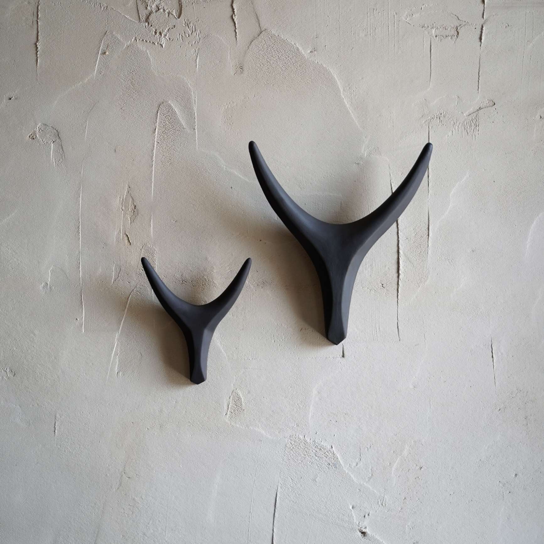 Two black antler-shaped wall hooks on a textured light gray wall.