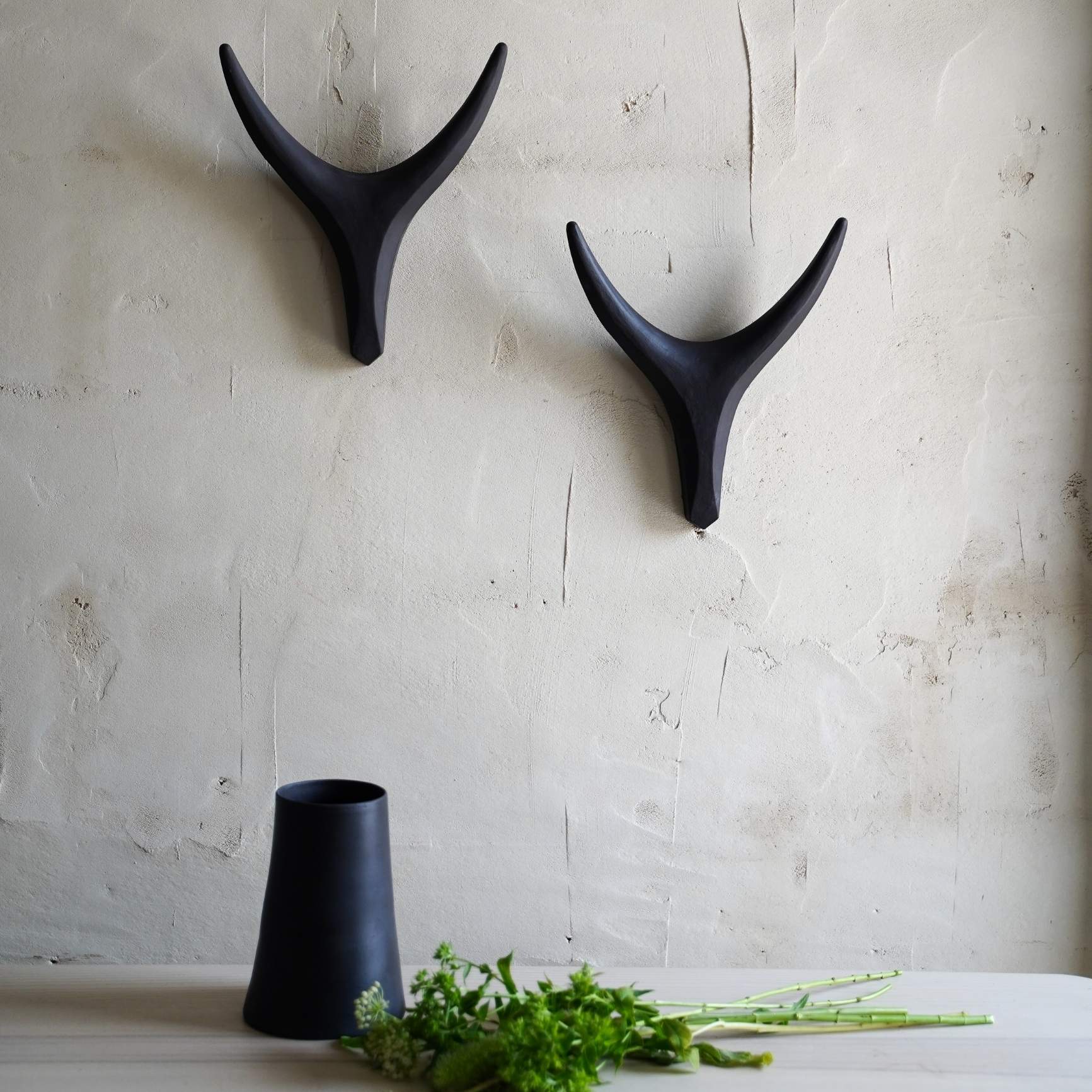 Handmade black ceramic antler wall decor mounted on textured wall, modern minimalist home styling.