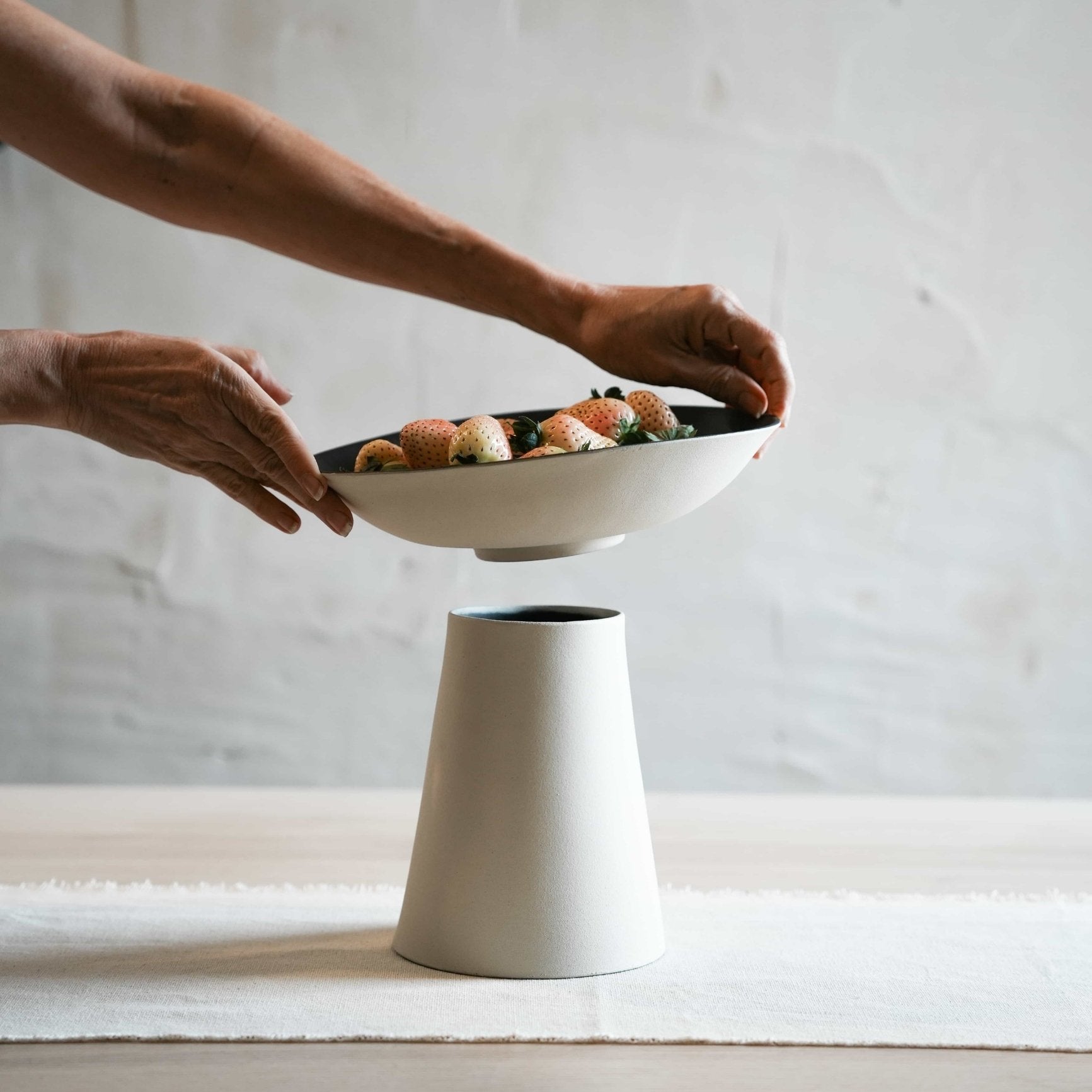 Person holding a white ceramic bowl with food on a neutral background