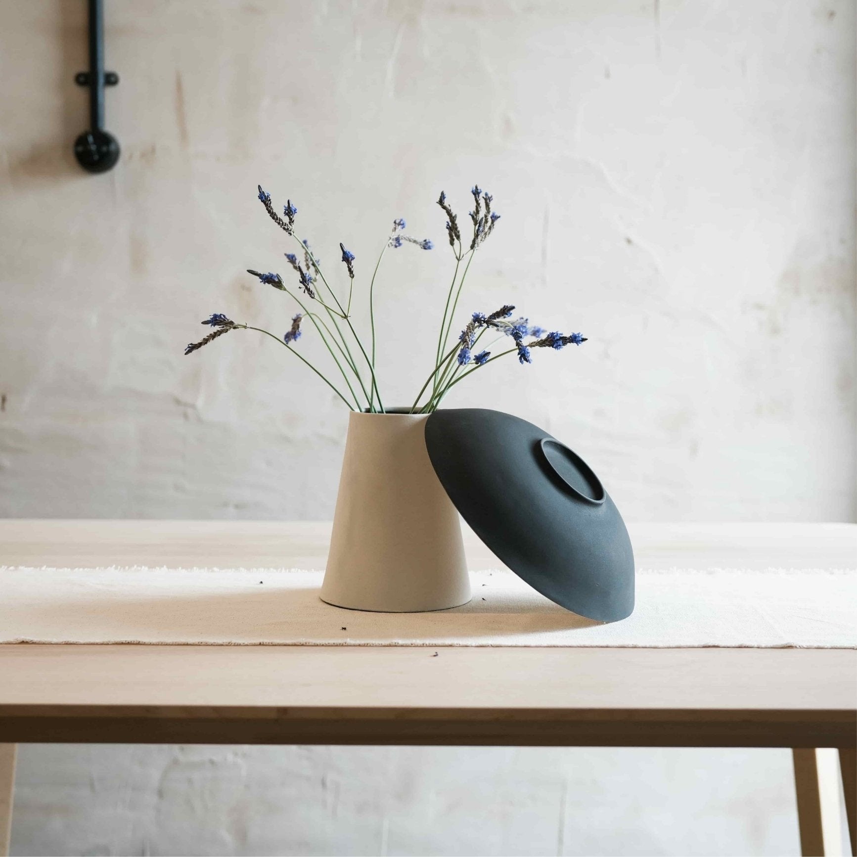 A white vase with flowers and a bowl on a wooden surface with a light background.