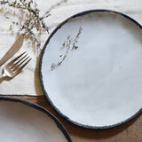 white ceramic salad plate with black rim with fork and white cloth