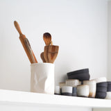 white crumpled vase with utensils, next to other pottery