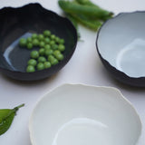 three black and white ceramic bowls with natural, jagged edges. Photographed from an upper angle and displayed with green peas