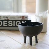 decorative black bowl with legs photographed from a profile view and styled with a candle and design materials in the background