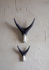 Two black and white decorative cearmic antlers wall hooks on a textured beige wall.