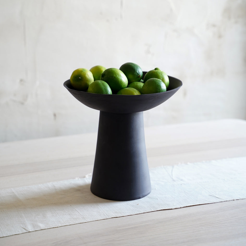 Black ceramic pedestal bowl holding fresh fruit, modern kitchen countertop decor