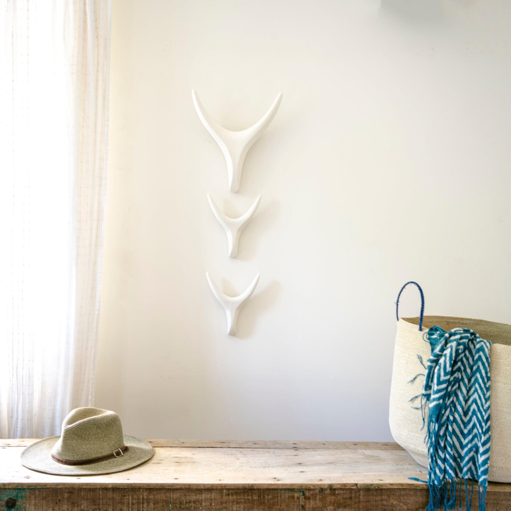 White antler wall decor above a wooden bench with a hat and basket.
