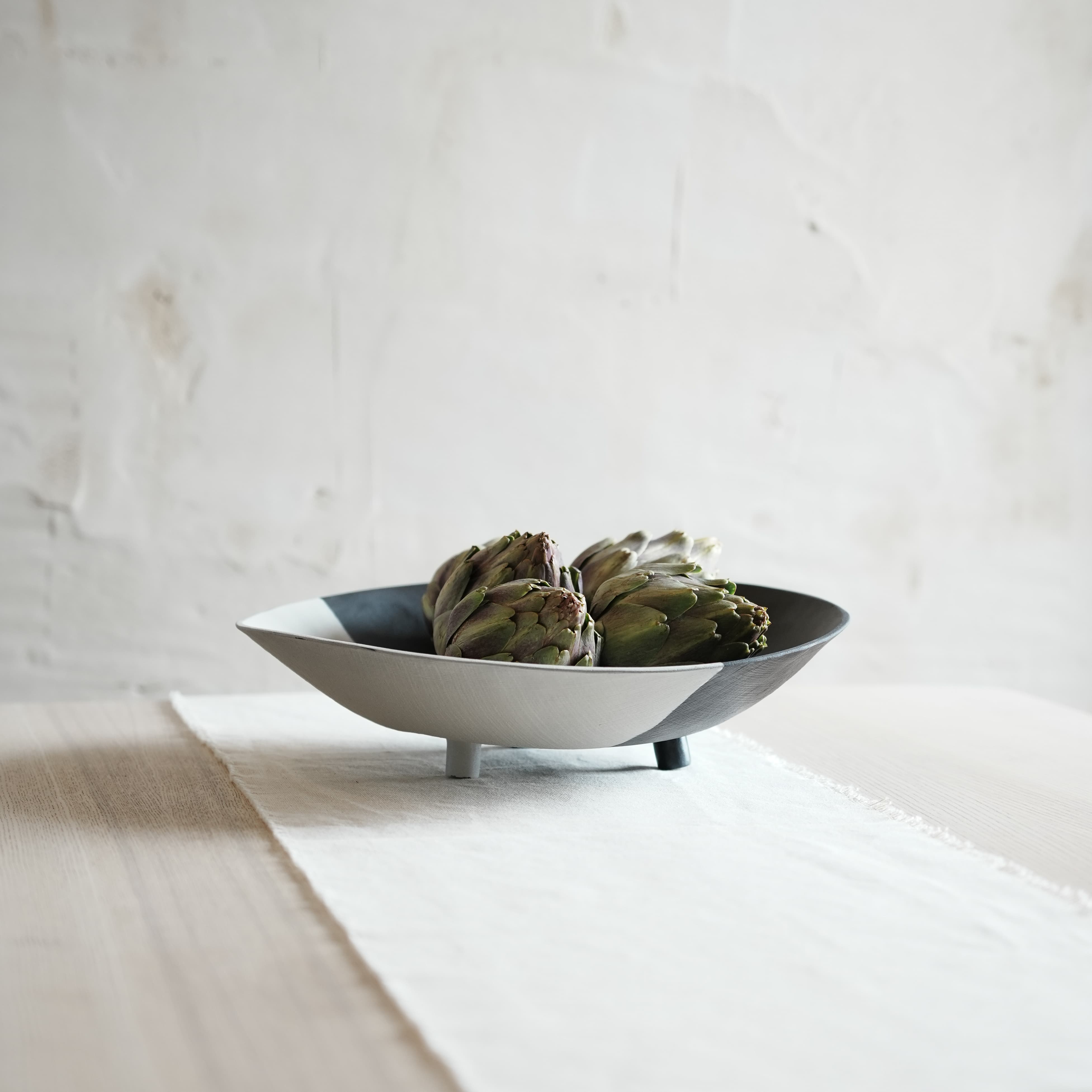 Black and white bowl with artichokes on a light surface and background