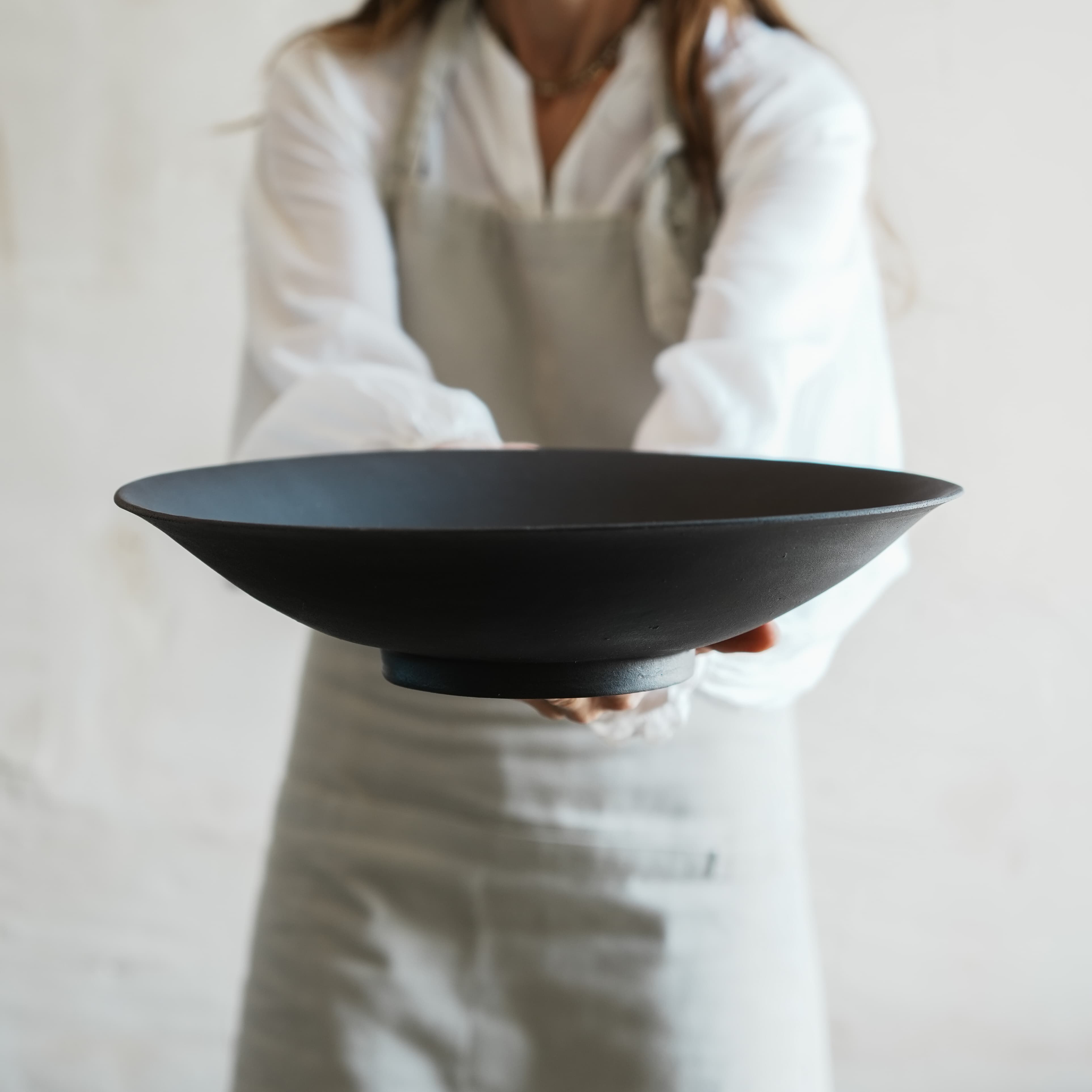 Handmade black stoneware pedestal bowl held by hand, minimalist ceramic bowl with matte finish