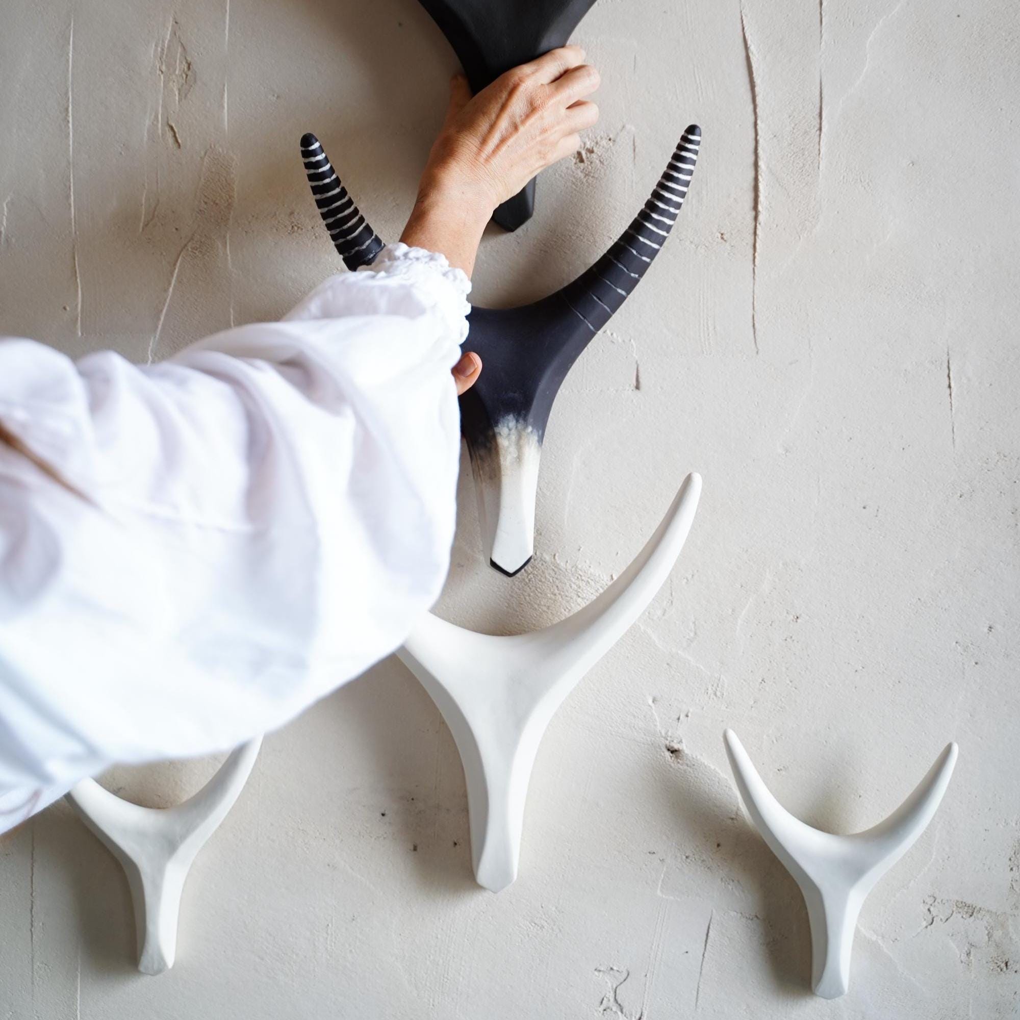 Close-up of a hand installing a black ceramic antelope horn wall sculpture