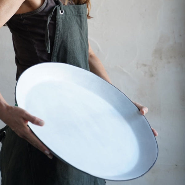woman wearing an apron holds a large white plate