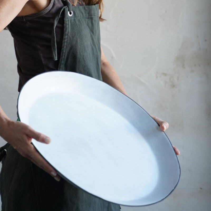 woman wearing an apron holds large white platter with black rim