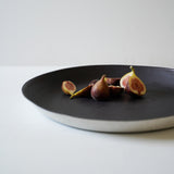 a few small figs in a large black shallow circle tray with a white rim