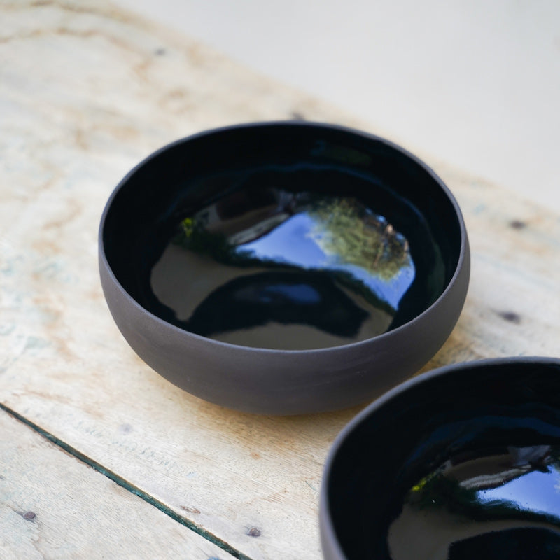 Black ramen bowls photographed from a high angle. The exterior is matte and the interior is a dark shiny black