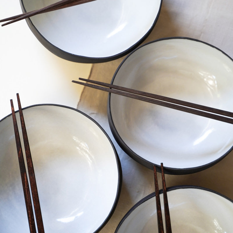 set of four black ramen bowls with white interiors, each with a set of chopsticks, photographed from an aerial position.