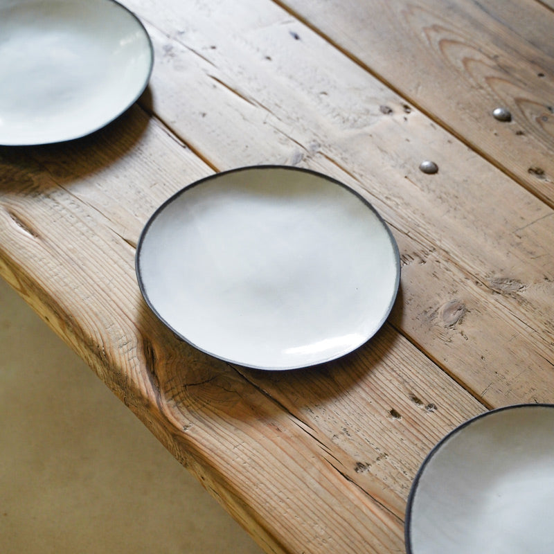 three organic, ceramic white plates with black rims placed on a wooden table