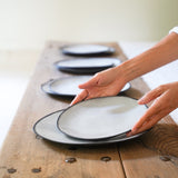 hands set a table of medium black stoneware plates on top of large black stoneware plates.