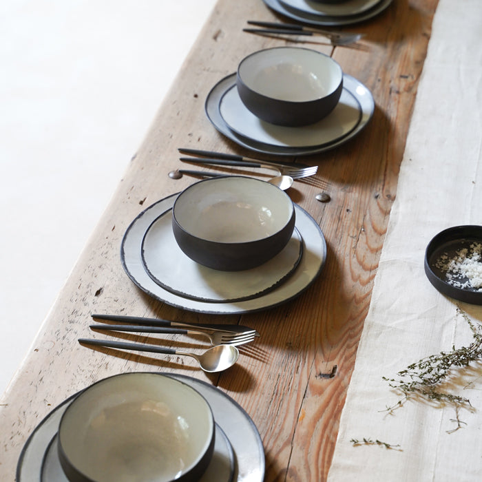 A set table for four. Each placement has two plates, a bowl and a set of utensils.