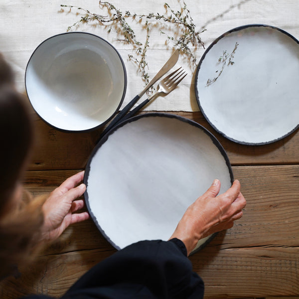 a woman lays two different plates and one bowl on a table, aesthetically photographed from an aerial position