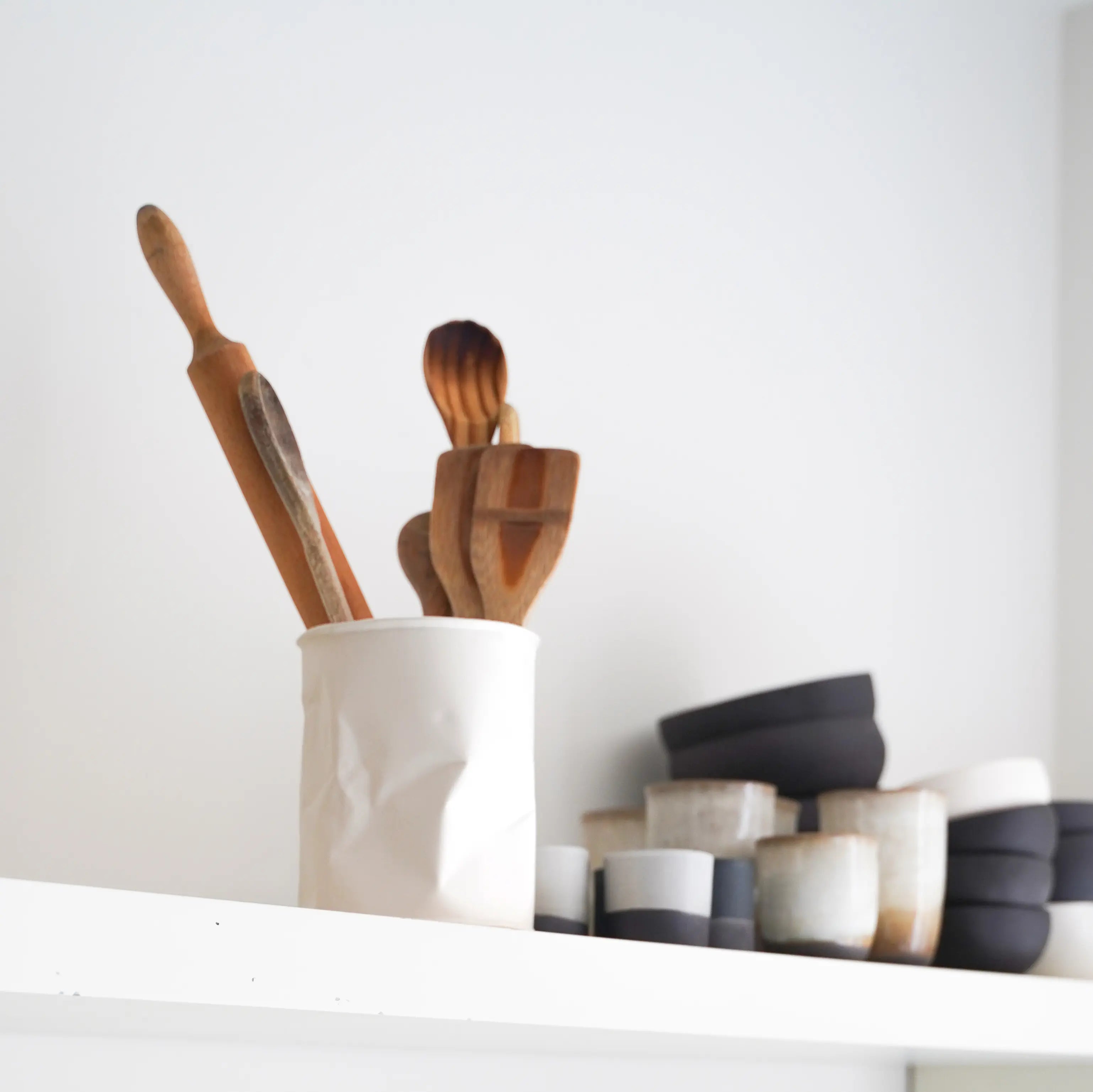 white crumpled vase with utensils, next to other pottery