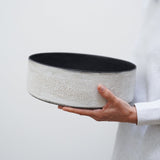 woman holds a large ceramic cylinder bowl with a matte black interior and a naturally textured matte white exterior
