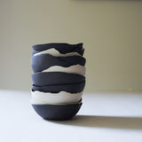 a stack of raw-edged ceramic black and white bowls, photographed from the profile view