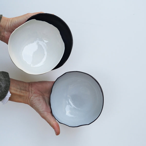 two hands hold three black and white decorative ceramic bowls with natural edges, photographed from an aerial view