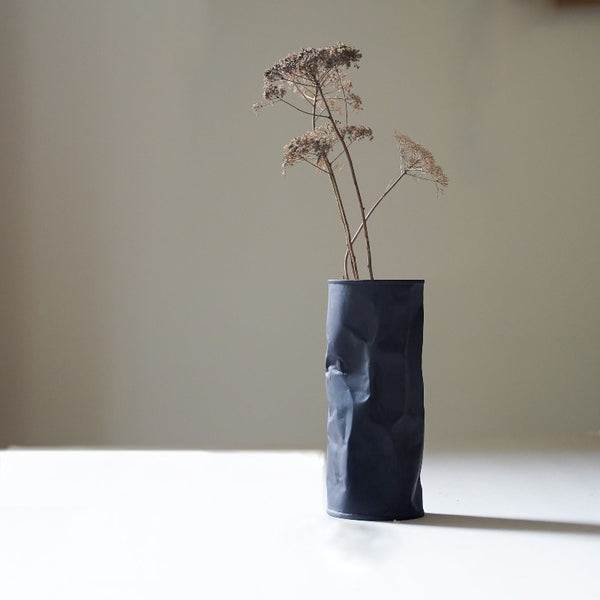 black crumpled bud vase with a few flowers
