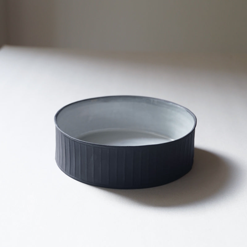 black and white cylinder bowl with an exposed, ribbed black stoneware exterior and a white glossy interior