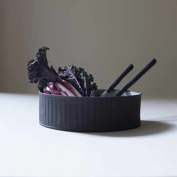ceramic cylinder salad bowl serving purple lettuce and styled with ceramic serving spoons. The outer walls are black, matte and ribbed, and the interior is a milky white