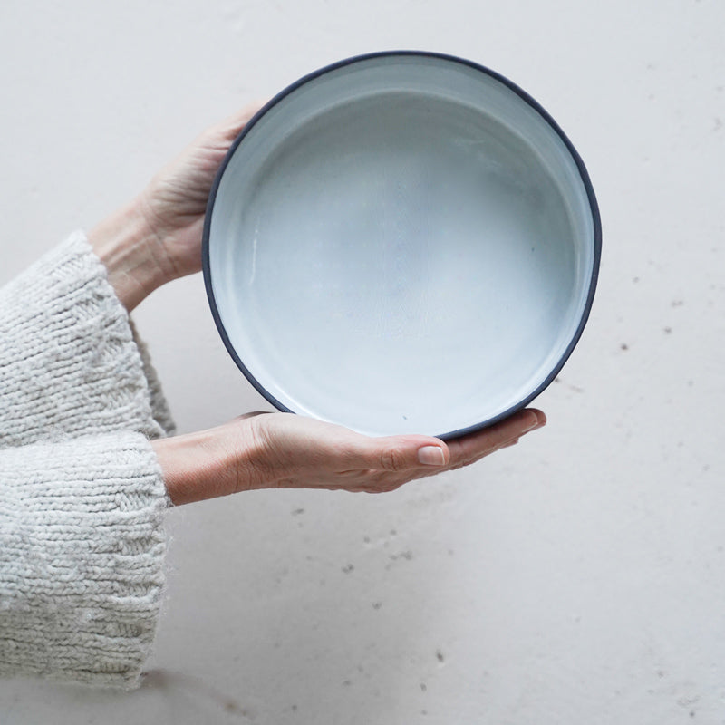 hands hold a black and white cylinder bowl. photographed from the aerial position. The interior is a glossy white and the rim is visible as exposed black stoneware