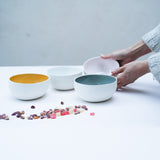 woman places four porcelain pastel bowls