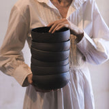 woman holds a tall stack of elegant, black ramen bowls