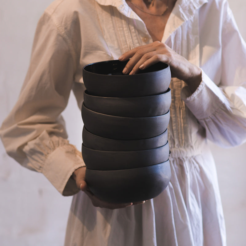 woman holds stack of black hand made ramen bowls