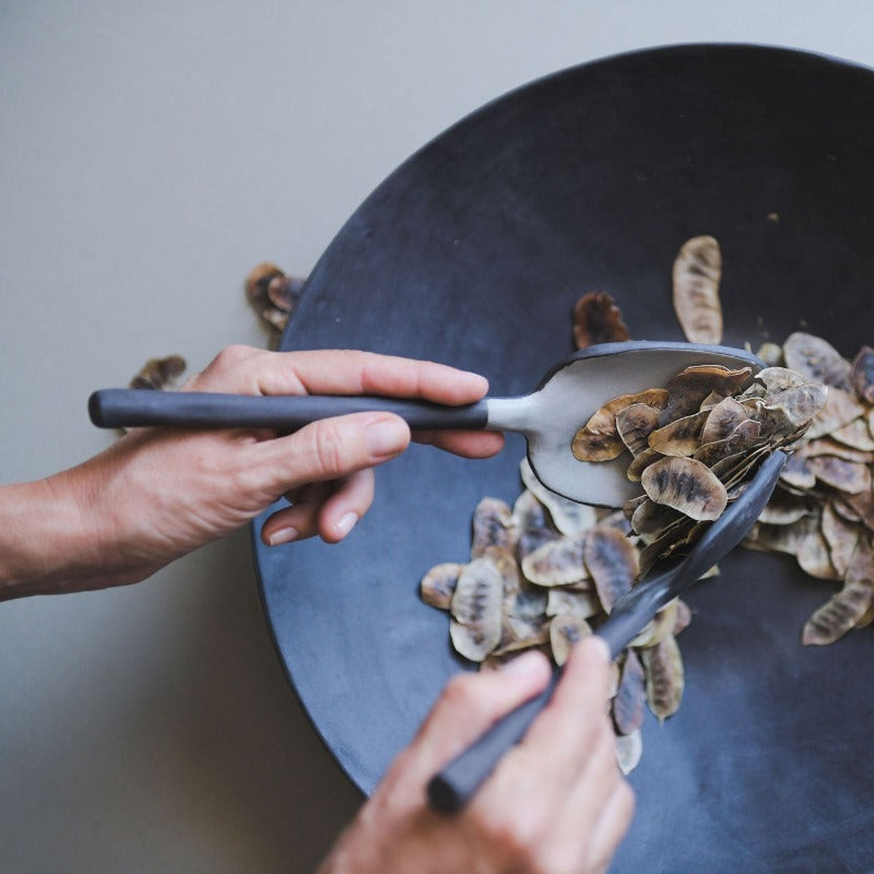 hands using ceramic tongs to pick up leaves in a bowl