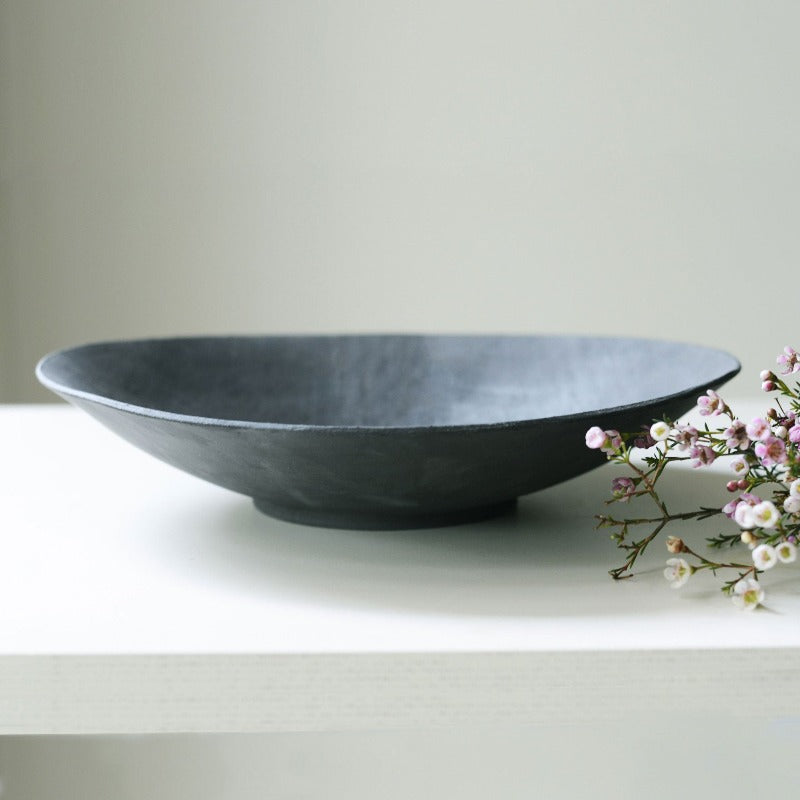large black decorative bowl photographed at an angle and styled with pink flowers