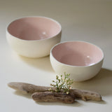 two pink coconut bowls, white matte on the exterior and glossy baby pink on the interior. Styled with a  branch and white flower