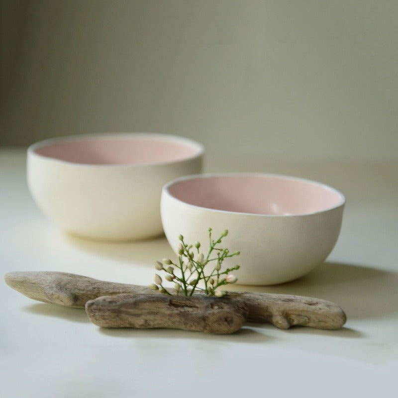 two porcelain  bowls with pink interior. styled with a branch and flower. photographed from a distance