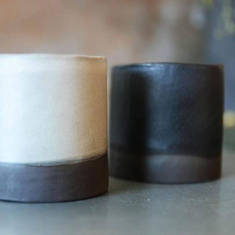 two black stoneware double espresso cups, one glazed white and one glazed black. Both with an exposed base