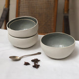 a stack of white porcelain bowls with a mint interior next to a single bowl, a spoon and spices