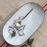 aerial view of a white stadium oval platter with a black rim artistically posed with a spoon and black twigs