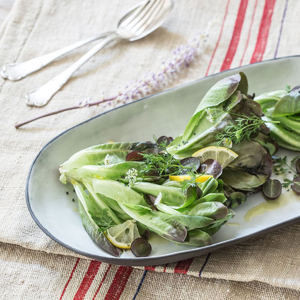 elegant salad plated in wide oval white tray with a black rim