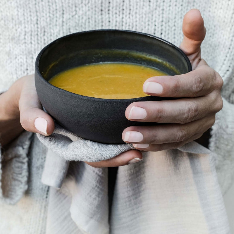 hands holding black ceramic bowl with pumpkin soup