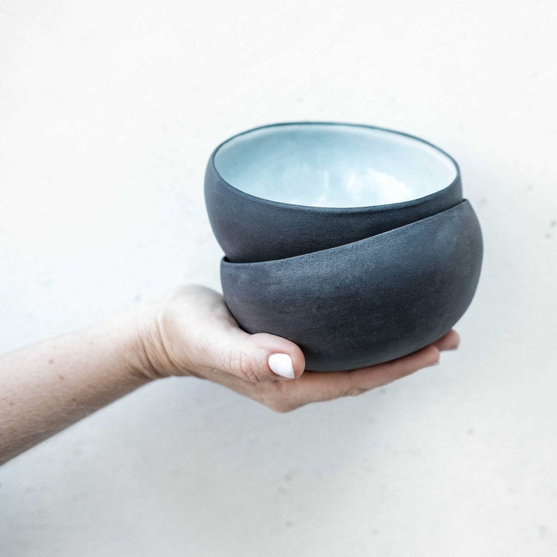 a hand holds out two "white coconut bowls" stacked - black matte on the exterior and white glaze on the interior