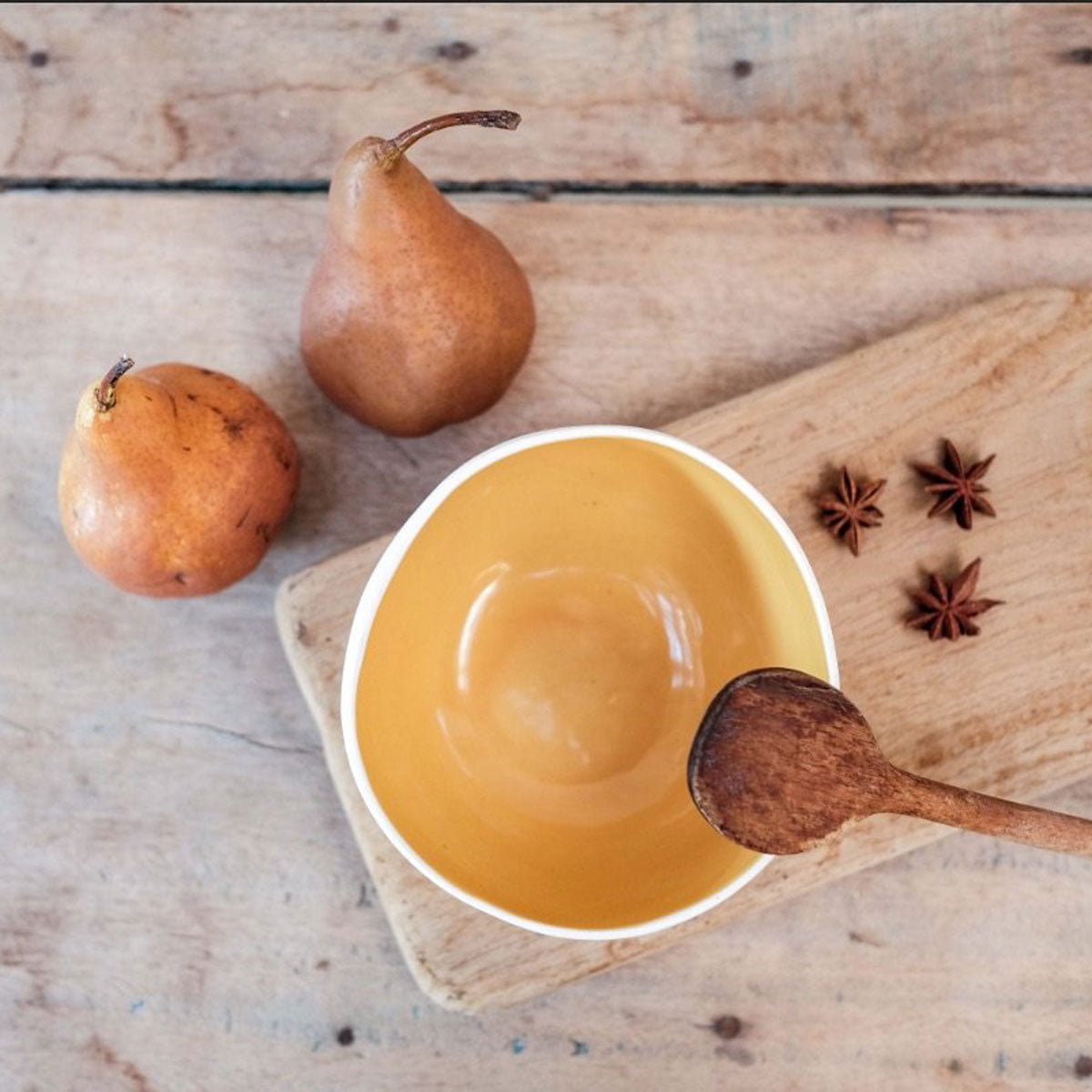 One porcelain coconut bowl with a yellow glaze interior photographed from the aerial position. placed on a cutting board with anise flowers and styled next to two pears